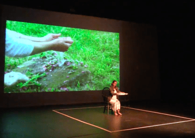 Luisa Bieri in performance on a stage with image projected behind her