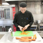 Chef Isaac DeLamatre, wearing black, cuts carots in the Birch Kitchen