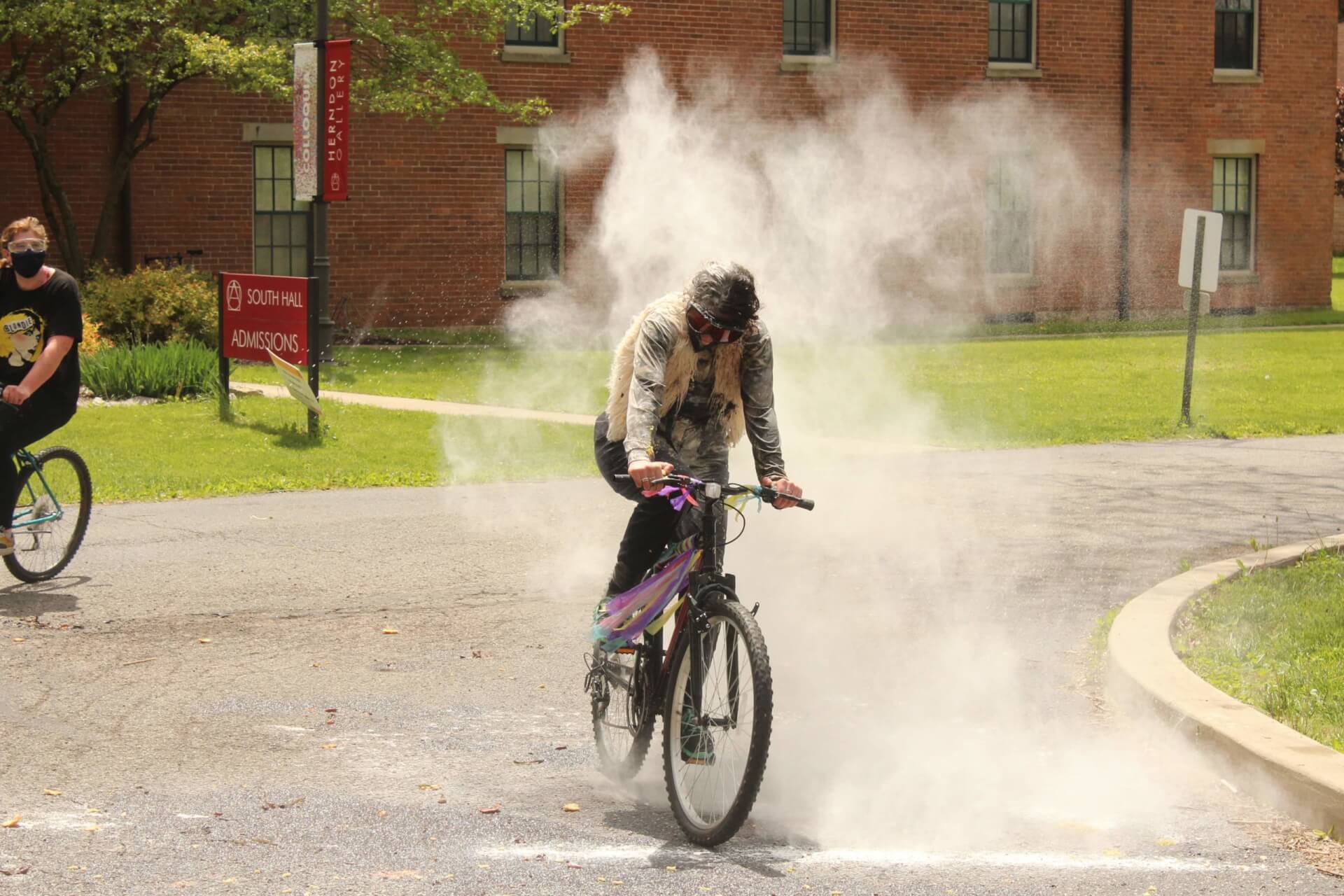A rider on the Horseshoe looks on as another bike rider moves through a cloud of flour that was thrown at them.