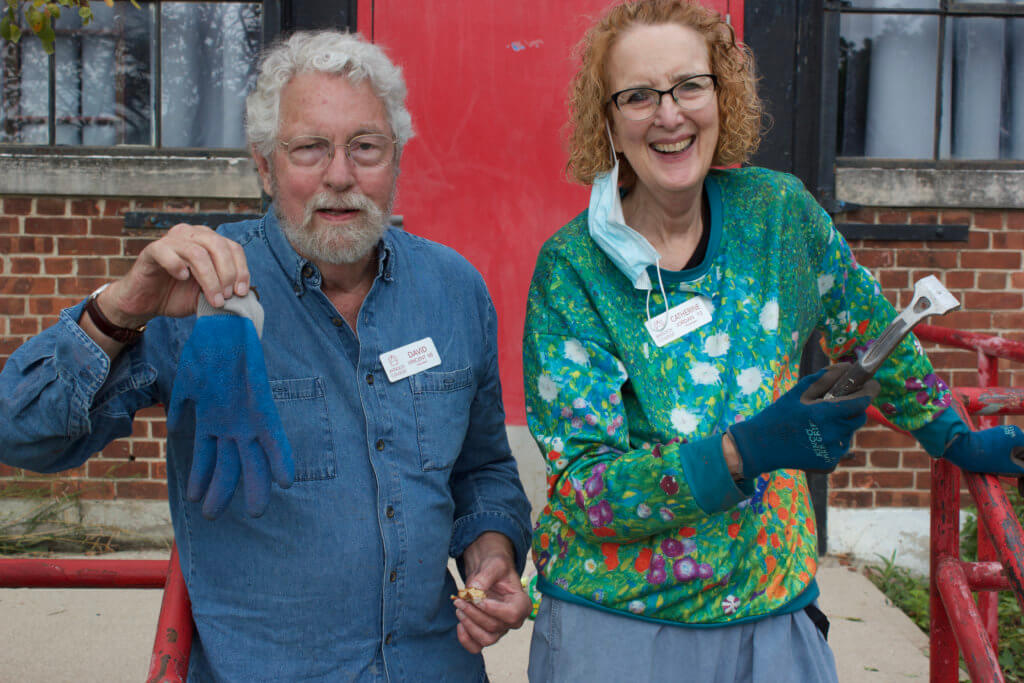David Vincent class of 1965 and Catherine Jordan class of 1972 smiling in front of the Foundry Theater while scraping old paint off the railings out front during the Volunteer work Party 2021