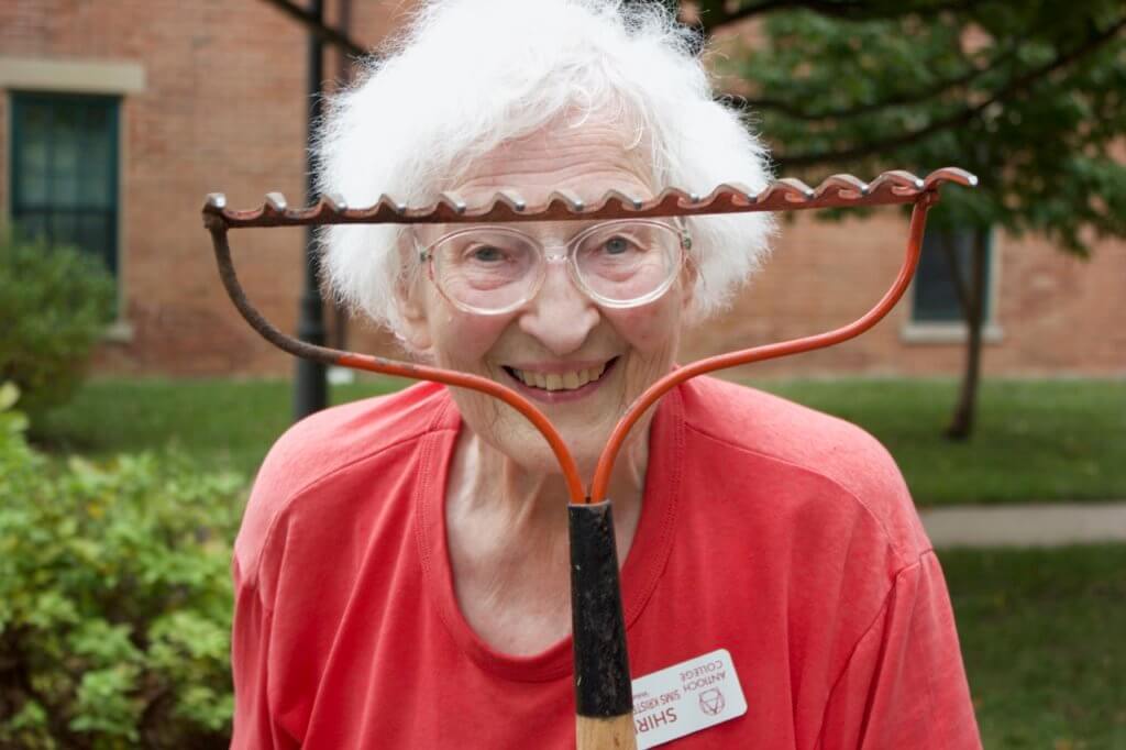 Shirley Kristensen class of 1954 playfully smiles for the camera while looking through a rake during the Volunteer Work Project 2021