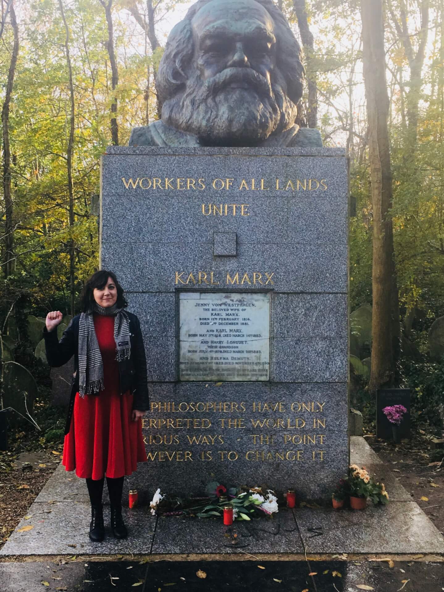 Professor Natalie Suzelis stands with a raised fist next to the massive marble tombstone of Karl Marx