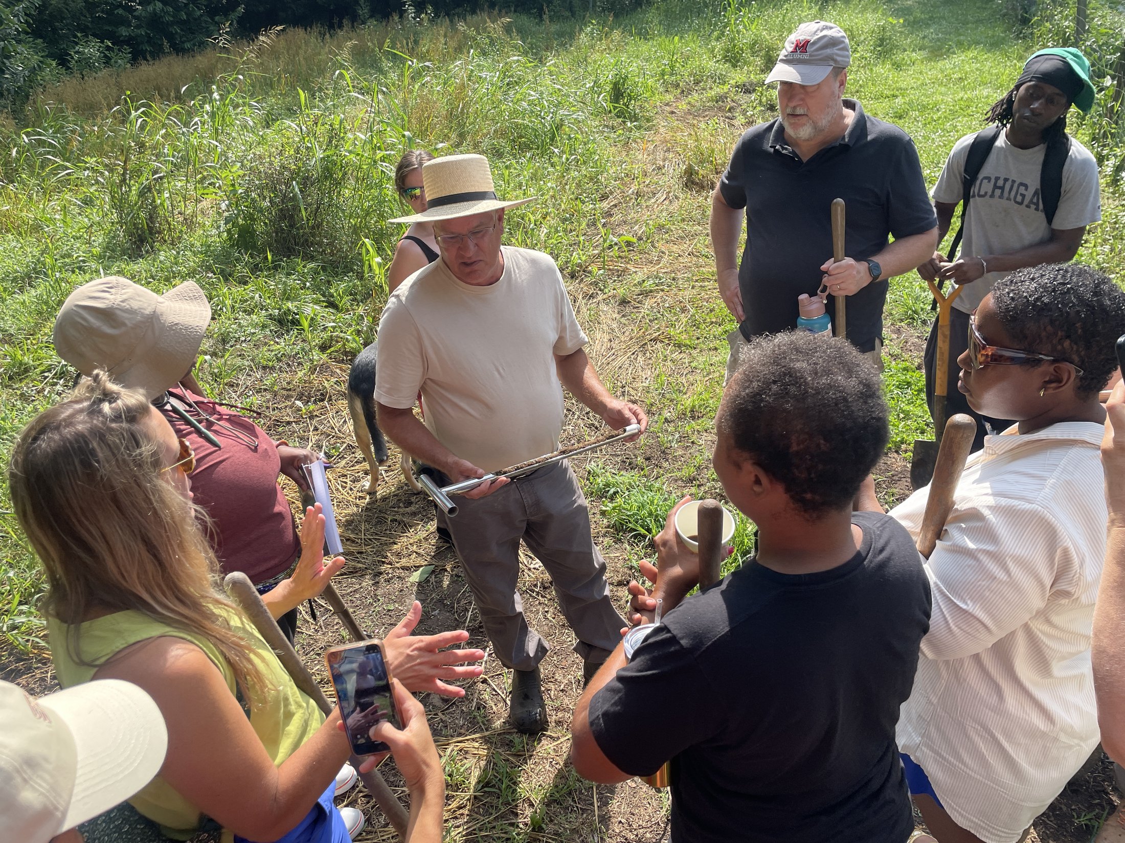 Program participants gathered around an instructor demonstrating a soil probe in a field