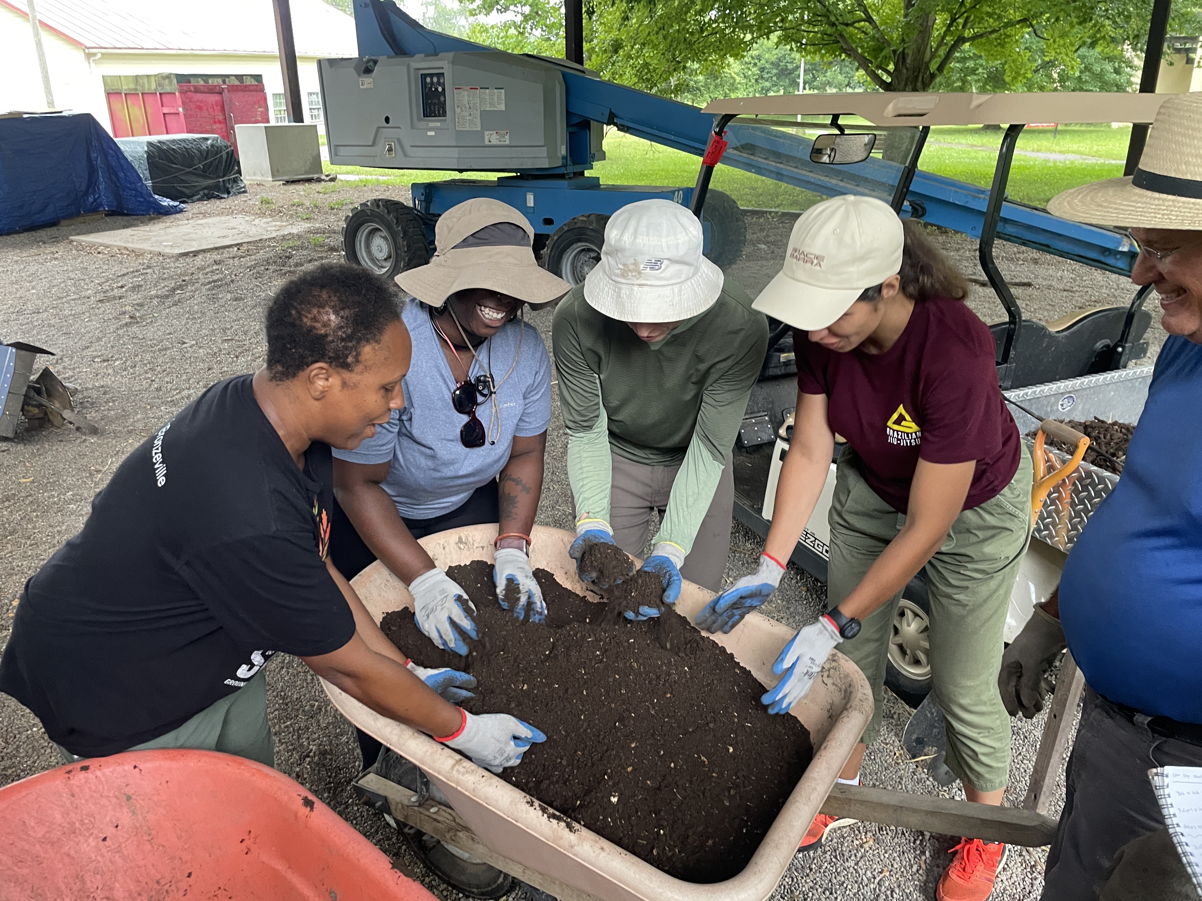 Group examining and mixing compost soil in a wheelbarrow